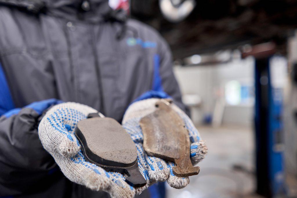 Mechanic hands with brakes pads, one is old fully worn and the other one is new