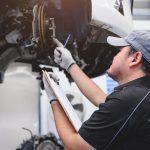 Mechanic with a clipboard inspecting brakes on a vehicle on a lift.