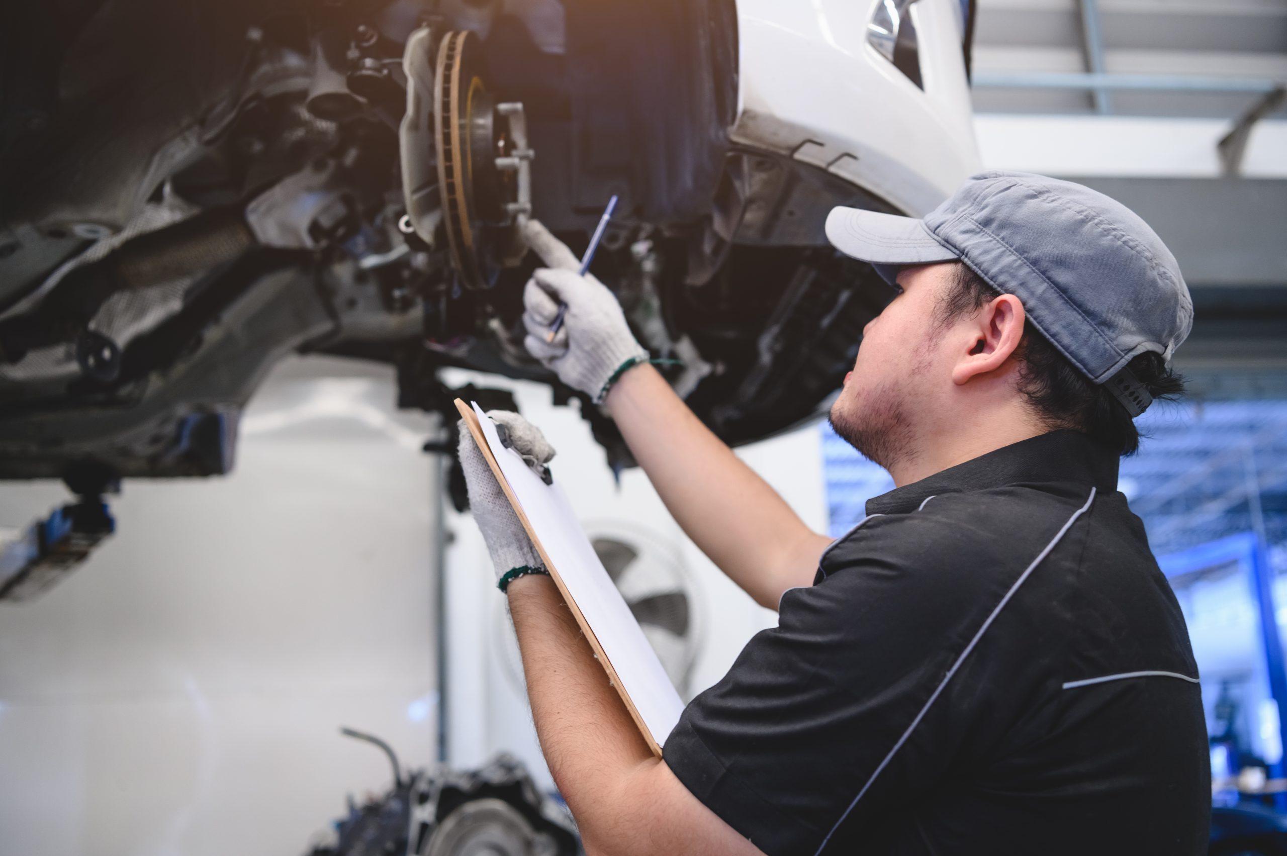 Mechanic with a clipboard inspecting brakes on a vehicle on a lift.